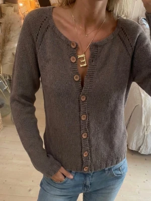 Brun stickad kofta med träknappar - Mysig brun stickad kofta med långa ärmar och träknappar framtill. Koftan har en rundad halsringning och ribbade muddar vid ärmslut och nederkant. Perfekt att slänga över en t-shirt för en avslappnad look.