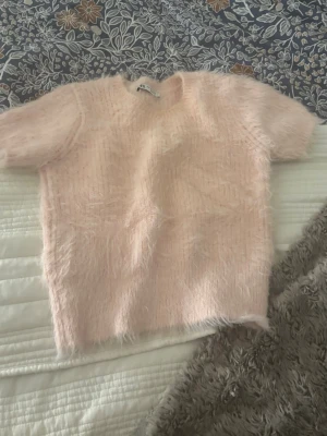 Ljusrosa fluffig stickad tröja - Supersöt ljusrosa stickad tröja med korta ärmar och fluffig, mjuk textur. Perfekt för dig som gillar en cozy och trendig look. Rund halsringning och rak passform. Passar till både jeans och kjol.