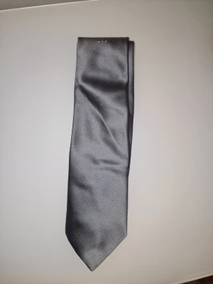 Silvergrå slips från Odd Fellow - Stilren silvergrå slips från Odd Fellow i glansigt tyg. Klassisk design som passar till skjorta och kavaj. 