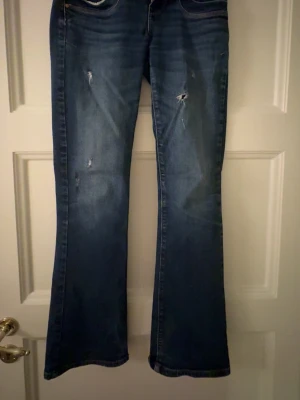 Blå bootcut jeans med slitningar -  Säljer mina så snygga jeans som tyvärr blivit för små för mig. Snygga blå bootcut jeans med slitningar framtill och klassisk femficksdesign. Jeansen har en mörk tvätt och lätt utsvängda ben. Perfekta för dig som gillar en avslappnad men trendig stil. Bara att fråga om du undrar något eller vill se fler bilder! Pris kan diskuteras💞