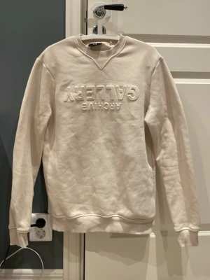 Beige sweatshirt från C&A - Säljer en beige sweatshirt från C&A med broderad text 'ARCHIVE GALLERY' på bröstet. Tröjan har rund halsringning, ribbade muddar och är tillverkad i mjukt material. Perfekt för en chill o lite schysstare stil