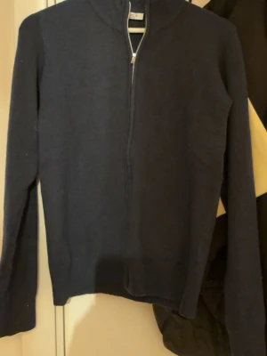 Mörkblå halvzip tröja - Mörkblå stickad tröja med halv dragkedja och hög krage. Tröjan har lång ärm och en enkel, stilren design som passar perfekt till lager-på-lager. Materialet ser ut att vara mjukt och bekvämt, perfekt för kyligare dagar.