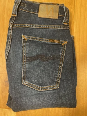  Nudie Jeans - Snygga mörkblå jeans från Nudie Jeans med klassisk femficksdesign. Jeansen har en slim fit passform. Jeansen hade ett hål vid skrevet som vi då skickade in och fråga om de kunde lösa det. Tyget syns knappast.w29 L32
