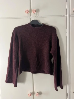 Mörklila stickad tröja med rund hals - Mysig mörklila stickad tröja med rund halsringning och långa ärmar. Tröjan har en rak och något boxig passform, perfekt för lager-på-lager. Materialet ser ut att vara mjukt och fluffigt, vilket ger en avslappnad vibe.