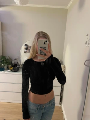 Svart croppad långärmad topp - Snygg svart croppad topp med långa ärmar och rund halsringning. Toppen har en tight passform och är gjord i ett mjukt, stretchigt material som sitter skönt på kroppen. Perfekt att styla med jeans eller kjol för en trendig look.
