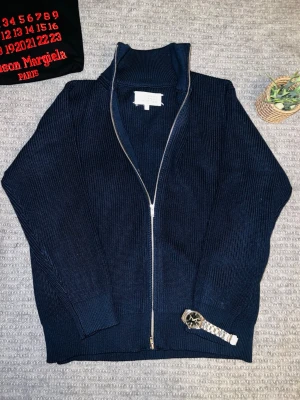 MM14 fullzip - Mörkblå Maison Margiela Full-zip tröja🧵  Tröjan har inga defekter, såsom fläckar eller hål. Den har max använts 3 gånger och är mycket skön🧸 På bilderna ser den mörkare ut.  Mått 📏(cm) Längd: 65 Bröst: 58 Axelbredd: 45  Tveka inte att fråga om plagget, är aktiv ofta Skickar inom 48 timmar📦