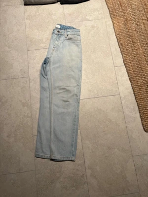 Ljusblå raka jeans från Grunt - Säljer ett par ljusblå jeans från Grunt med klassisk femficksdesign och raka ben. Jeansen har normal passform och är tillverkade i jeansmaterial med snygga kontrastsömmar. Perfekta för en avslappnad och trendig look.