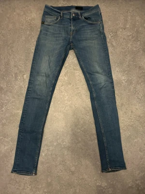 Blå skinny jeans med klassisk look från tiger of Sweden - Snygga blå skinny jeans med klassisk från tiger of Sweden femficksdesign och smal passform. Jeansen har normalhög midja och är tillverkade i ett stretchigt denimtyg som sitter tajt längs benen. Perfekta för en stilren och enkel vardagsstil.