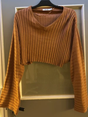 Brun croppad ribbad tröja - Säljer en brun croppad tröja med breda, utsvängda ärmar och ribbad struktur. Tröjan har V-ringning och är gjord i ett mjukt stickat material. Perfekt för dig som gillar trendiga och bekväma plagg.
