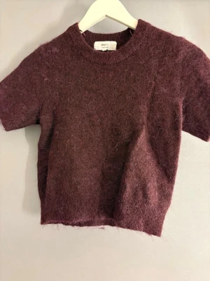 Vinröd stickad tröja Gina Tricot - Mysig vinröd stickad tröja från Gina Tricot i alpackablandning. Tröjan har korta ärmar, rund halsringning och en fluffig, mjuk struktur som ger en trendig look. Perfekt att styla med jeans eller kjol för en avslappnad vibe.