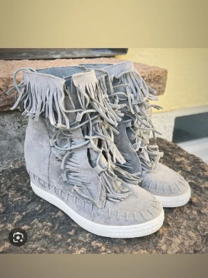 Isabell marant liknade skor perfekta till våren - Unika vita sneakers i mocka med högt skaft och coola fransdetaljer runt hela skon. Skorna har snörning och en platt sula, vilket ger en avslappnad men ändå trendig look. Perfekta för dig som vill sticka ut med din stil. Dem är använda typ 2 gånger så dem är väldigt fräscha och ser nya ut. 
