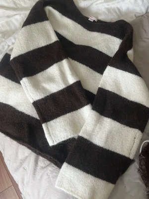 Randig stickad tröja från Gina Tricot - Stickad tröja från Gina Tricot med breda bruna och vita ränder. Tröjan har en avslappnad passform, rund halsringning och långa ärmar.  Materialet är mjukt och fluffigt. Använd bara 1 gån därav som ny!🤍