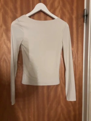 Ljusbeige långärmad topp med öppen rygg från Bikbok - En stilren ljusbeige topp med lång ärm och en snygg, djup urringning i ryggen. Toppen har en tight passform och är tillverkad i ett mjukt, stretchigt material som sitter skönt mot kroppen. Perfekt att matcha med jeans eller kjol. Super bra skick 