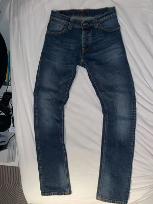 Nudie grim Tim jeans - Snygga blå Levi's 511 jeans med slim fit och klassisk femficksdesign. Jeansen har en lätt tvättad look med subtila slitningar och orangea sömmar. Perfekta för dig som gillar en modern och stilren vibe. Materialet är klassisk denim i bomull.