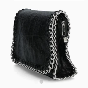 Svart axelväska med kedjedetaljer - Säljer en svart axelväska i skinn med grova silverfärgade kedjor längs kanterna och dragkedja upptill. Väskan har en cool och edgy look som verkligen sticker ut. Perfekt för dig som vill ha en statement piece till din outfit. Små defekter men inget som syns vid användning, vita fläckar på insidan