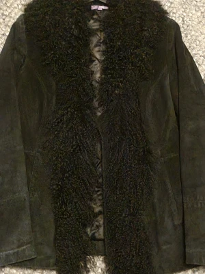 Svart mocka jacka med fuskpäls krage - Snygg, svart mocka jacka med långärmad design och fluffig fuskpäls krage och framkant. Jackan har en klassisk passform och lätt fodrad som ger en lyxig känsla. Perfekt för dig som vill sticka ut med en statementjacka.