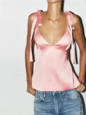 Rosa satintopp från zara - Supersött ljusrosa linne i satin med breda axelband som knyts på axlarna. Linnet har v-ringad urringning och en lätt croppad passform. Perfekt att styla med jeans eller kjol för en trendig look.