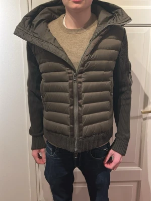 Mörkgrön cardigan från moncler - Snygg mörkgrön teddyjacka från Moncler med stickade ärmar och vadderad kropp. Jackan har huva, dragkedja framtill och en praktisk ficka med dragkedja på ärmen. Perfekt för dig som vill ha en trendig och bekväm look. Super bra sckick. M