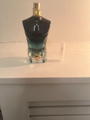 Le Male parfym från Jean Paul Gaultier - Ikonisk parfymflaska formad som en manlig torso från Jean Paul Gaultier. Flaskan har en snygg färgskiftning från svart till turkos och guldiga detaljer på korken. Perfekt för dig som gillar unika och stilrena doftflaskor.