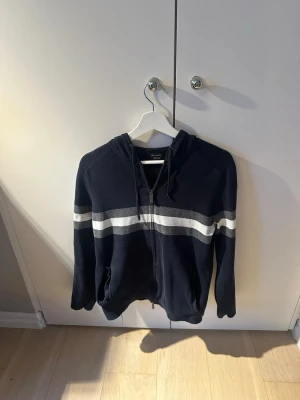 Mörkblå zip hoodie massimo dutti - Mörkblå hoodie med vit och ljusgrå horisontell rand över bröstet och ryggen. Tröjan har huva me, dragkedja framtill och två fickor. 