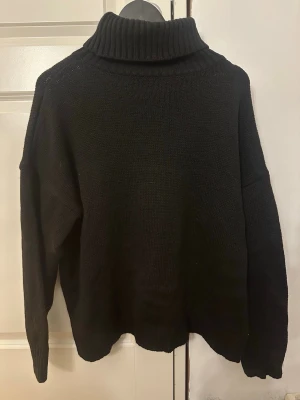 Svart stickad polotröja - Mysig svart stickad polotröja med hög krage och avslappnad passform. Tröjan har långa ärmar och ribbstickade muddar vid ärmslut och nederkant. Perfekt för kyliga dagar och enkel att matcha med olika outfits. Ingen lapp kvar, därav vet jag inte storlek eller märke. Sitter som en M