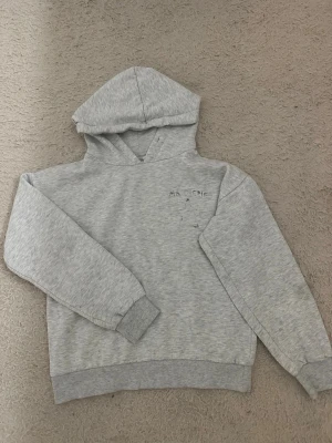 Grå hoodie med tryck 'Ma Chérie' - Ljusgrå hoodie med huva och trycket 'Ma Chérie' samt en stjärna på ryggen. Mjuk bomullskänsla och ribbade muddar vid ärmslut och nederkant. Perfekt för en avslappnad och trendig stil.