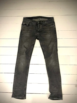 Grå jeans från Nudie  - Säljer ett par gråa slim fit jeans från Nudie Jeans med klassisk femficksmodell och diskreta slitningar. Storlek L32 W30. Ända defekten är det påsydda på sista bilden men det syns knappt vid användning och är inget man tänker på😉