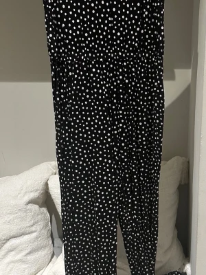 Svart prickig jumpsuit från H&M storlek S - Snygg svart jumpsuit med vita prickar och v-ringad rygg. Lätt och flowy modell med resår i midjan för skön passform. Perfekt för dig som gillar en lekfull och trendig stil. Materialet känns mjukt och svalt. 100% viskos 
