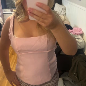 Ljusrosa linnetopp med rosett - Söt ljusrosa linnetopp med breda axelband och en stor rosett i ryggen. Toppen har en figurnära passform och är perfekt för varma dagar. Enkel och stilren design som passar till mycket.