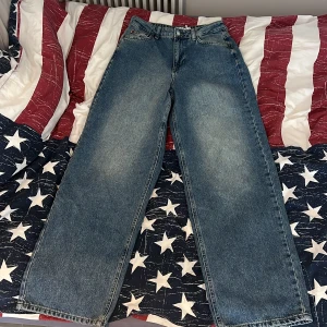 Mid blue loose low waist long jeans från NA-KD - Säljer ett par blåa jeans från NA-KD med loose passform och låg midja. Modellen är lång och har raka, breda ben. Klassisk femficksdesign, dragkedja och knapp framtill. Materialet är jeans med snygg tvättad look. Aldrig använts då dom inte passar mig. Exklusiva jeans då dom är exemplar som inte använts och finns bara ett exemplar! Etiketten sitter kvar på jeansen. 