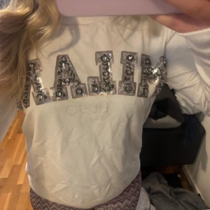 Vit långärmad topp från Liu Jo - Säljer en vit långärmad topp från Liu Jo med stora glittriga paljettdetaljer som stavar 'MILAN' på bröstet. Toppen har en klassisk rund halsringning och är perfekt för dig som gillar att sticka ut med lite extra bling.