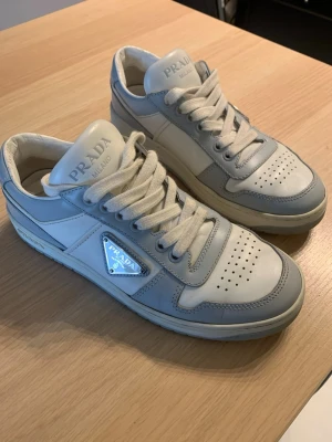 Prada vita och grå downtown sneakers - Snygga sneakers från Prada i bra skick. Vita och gråa i kalvläder. Köpt på Prada i Sthlm, kvitto finns samt skolåda. Nypris 11 100. Möts helst upp i Stockholm 