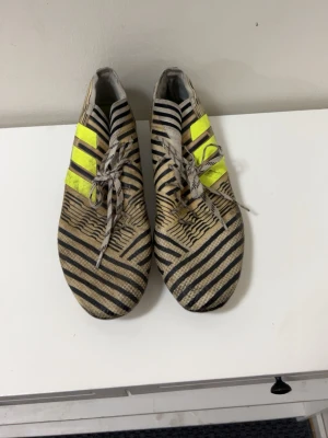 Adidas fotbollsskor med zebramönster - Snygga fotbollsskor från Adidas med zebramönster i svart och beige samt gula detaljer på sidorna. Skorna har snörning och dobbar för spel på gräs. Perfekta för dig som vill sticka ut på planen.