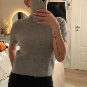 Grå stickad tröja från Zara - Supermjuk grå stickad tröja från Zara med kort ärm och rund halsringning. Enkel och stilren modell som är lätt att matcha till olika outfits. Perfekt för lager-på-lager under kyligare dagar.
