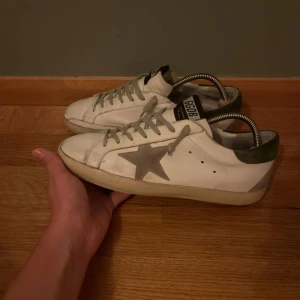 Vita Golden Goose sneakers med stjärna - Säljer ett par vita Golden Goose sneakers med grå mockadetaljer och ikonisk stjärna på sidan. Skorna är i storlek 41 och är i nästan helt nyskick, är perfekta för hösten. Säljs av oss för 1699kr, priset kan diskuteras.