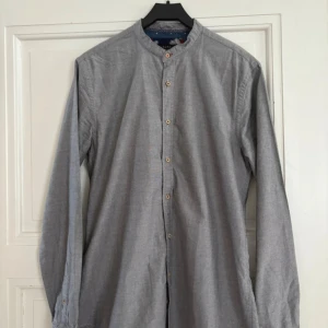 Grå henley-skjorta från Zara - Säljer en grå henley-skjorta från Zara i relaxed fit. Skjortan har ståkrage, långa ärmar och knappar framtill. Tillverkad i mjuk bomull, perfekt för en chill och stilren look. Enkel att matcha med jeans eller chinos.