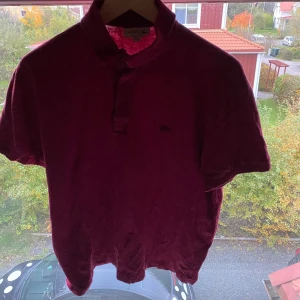 Vinröd pikétröja från Lacoste - Snygg vinröd pikétröja från Lacoste med klassisk krage och knäppning framtill. Ikoniska krokodilloggan broderad på bröstet. Tröjan är i regular fit och tillverkad i mjuk bomull med lite stretch för extra komfort. Perfekt för en stilren och avslappnad look.