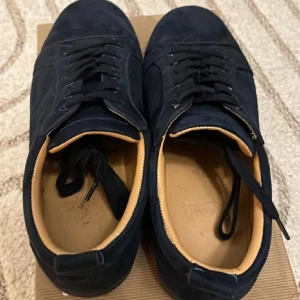 Louboutin skor  - Snygga mörkblå sneakers från Christian Louboutin i mocka med svarta snören och svarta sulor. Skorna har en stilren design med rund tå och beige innersula som ger en lyxig känsla. Perfekta för dig som vill ha något exklusivt och trendigt.