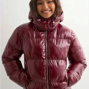 Jacka från Nelly  - Säljer en vinröd pufferjacka med glansig finish och huva från Nelly. Inte använd alls mycket.  Perfekt för kalla dagar nu på vintern och hösten! Pris kan diskuteras (org pris: 799kr)