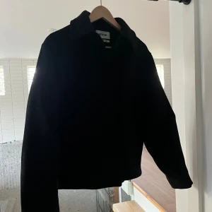 Svart overshirt från Weekday XS - Svart kort jacka från Weekday i stilren design med klassisk krage och raka långa ärmar. Jackan har en enkel look utan synliga detaljer. Perfekt för höstdagar. 