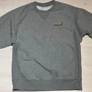Grå sweatshirt från Carhartt - Säljer en grå sweatshirt från Carhartt med broderad logga. Tröjan har rund halsringning med ribbade muddar och klassisk passform. Den är storlek xs men passar mer åt S. Inga defekter använd några gånger.