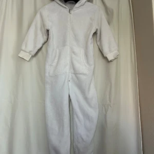 Vit fleece jumpsuit med huva - Supermjuk vit jumpsuit från Lindex i fleece med huva och dragkedja framtill. Har ribbade muddar vid ärmar och ben samt fickor på magen. Sötaste isbjörnen ❤️
