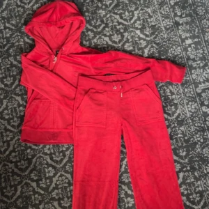 Juicy Couture röd velour hoodie - Juicy Couture hoodie i röd velour med dragkedja, huva och snörning. Klassisk logga broderad på bröstet och stora fickor framtill. Matcha med de tillhörande byxorna för en ikonisk 2000-talslook. Har använts 1 gång💗