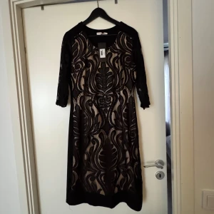 Svart paljettklänning - Säljer en svart långklänning med transparent mesh och detaljerat mönster i svart paljett. Klänningen har trekvartsärm och coola pärl- och paljettapplikationer som ger extra bling. Perfekt för dig som vill sticka ut med en unik look. Aldrig använd med etikett på