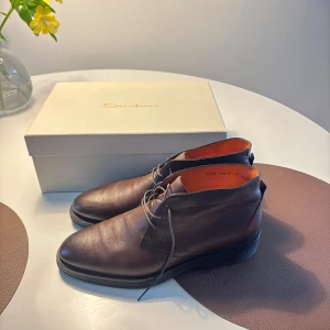Santoni Boots - Snygga bruna kängor från Santoni i äkta skinn med rund tå och platt sula. Klassisk design med snörning och orangefärgad insida. Perfekta för dig som gillar stilrena och tidlösa skor. Levereras med originalkartong och extra skosnören. Ny pris är runt 7000kr 