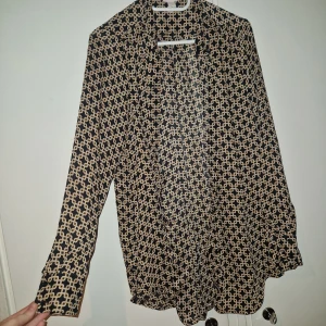 Skjorta - Snygg skjorta från Richard Allan x H&M. Svart botten med beige och brunt kedjemönster, klassisk krage och knappar framtill. Långärmad och tillverkad i mjukt, tunt material som känns skönt mot huden. Perfekt för dig som gillar coola retrovibbar.