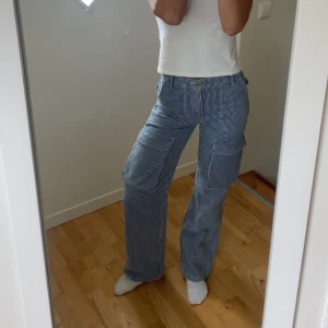 Randiga cargopants i blått och vitt - Säljer ett par blåvitrandiga cargopants med breda ben och stora fickor på sidorna. Byxorna har normal midja och raka ben. Perfekta för en chill och trendig look.