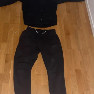 Svarta Nike mjukisbyxor XL - Svarta mjukisbyxor från Nike i storlek XL. Byxorna har en slim passform, resår i midjan med snörning och dragkedjeficka på ena benet. Tillverkade i mjukt bomullsmaterial, perfekta för chill eller träning. Diskret Nike-logga på benet.