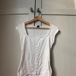 Vit topp med fyrkantig ringning Gina Tricot - Enkel och stilren vit topp från Gina Tricot med fyrkantig ringning och ärmlös design. Tillverkad i mjuk bomull, perfekt att matcha med jeans eller kjol. Snygg bas till garderoben för dig som gillar minimalistisk stil.