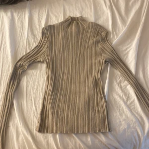 Beige ribbad polotröja från H&M - Säljer en beige/grön ribbad polotröja från H&M i storlek L. Tröjan är ny och nästan aldrig använd. Derför är den i topp skick. 